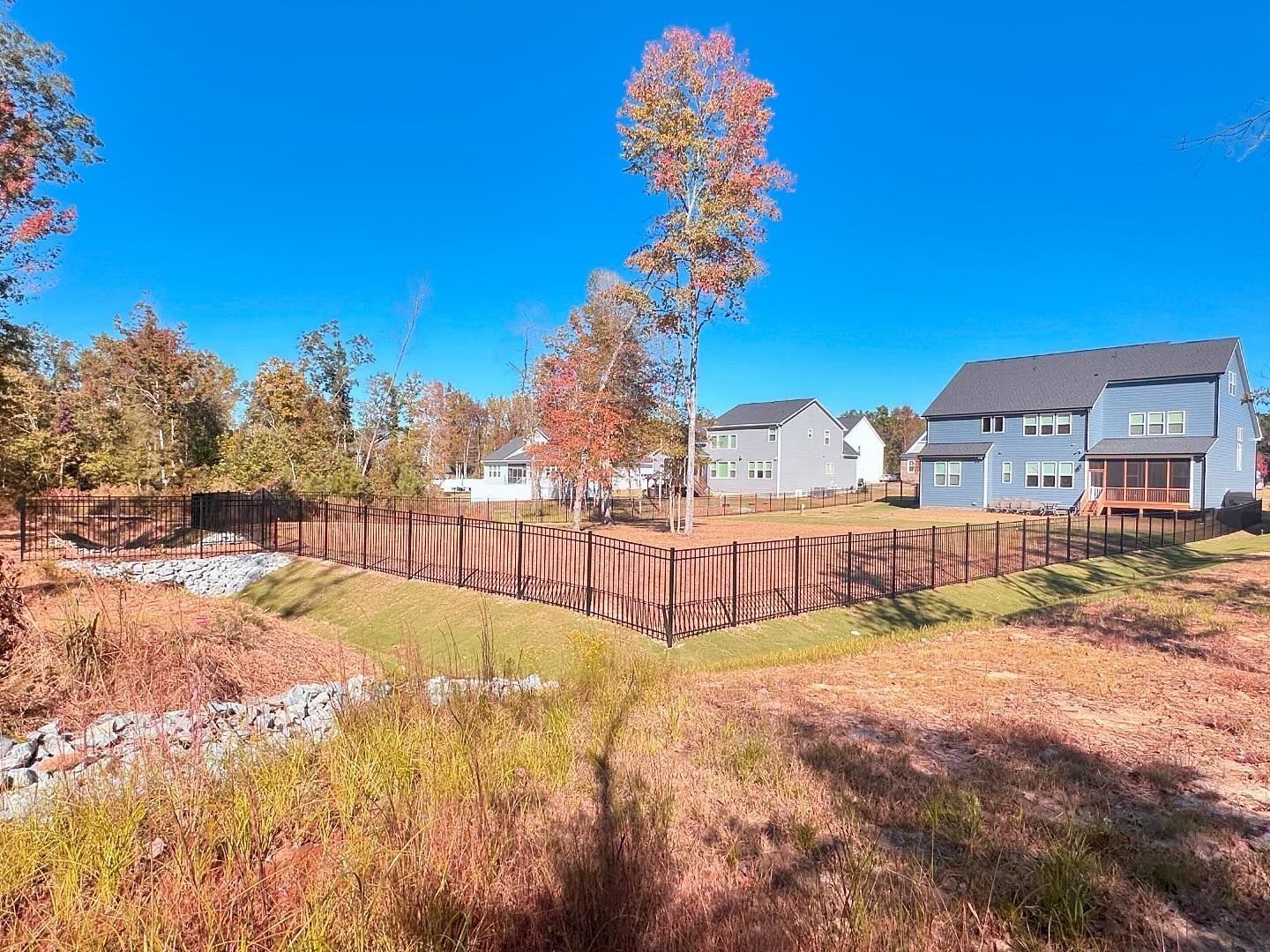 A wooden fence surrounds a lush green field with houses in the background.