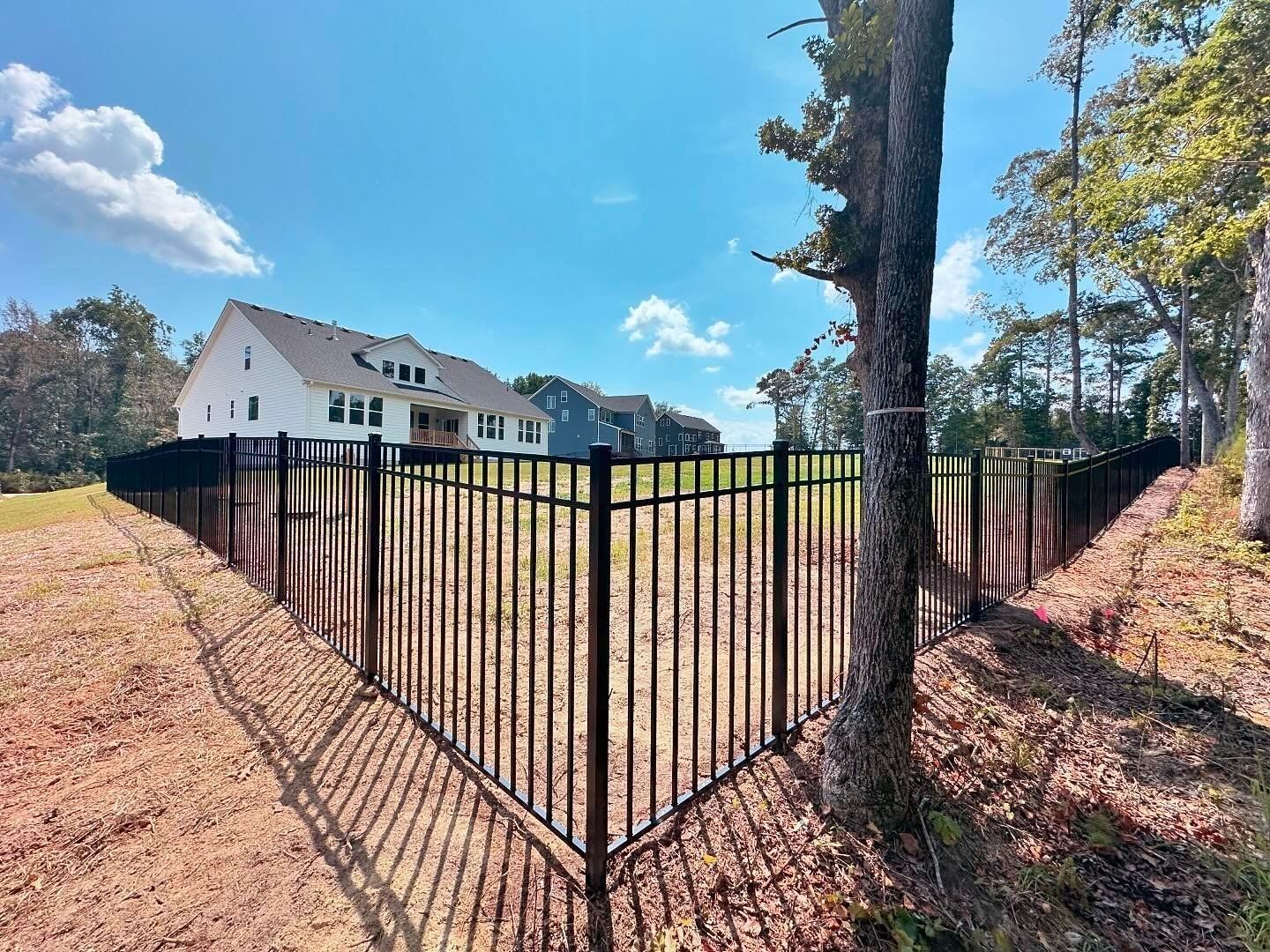 A black fence surrounds a large house in the middle of a field.