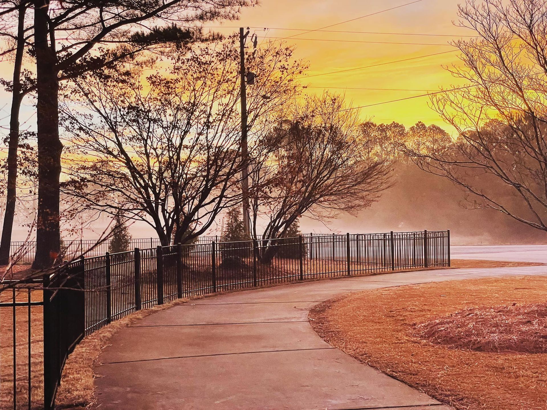 A fence along the side of a road with a sunset in the background