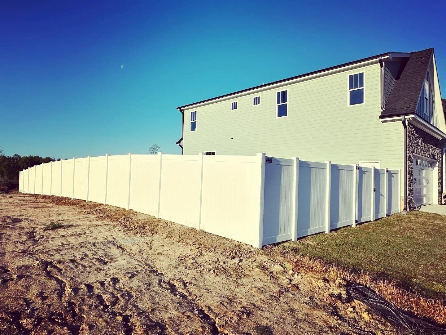 A white fence is surrounding a house in a dirt field.