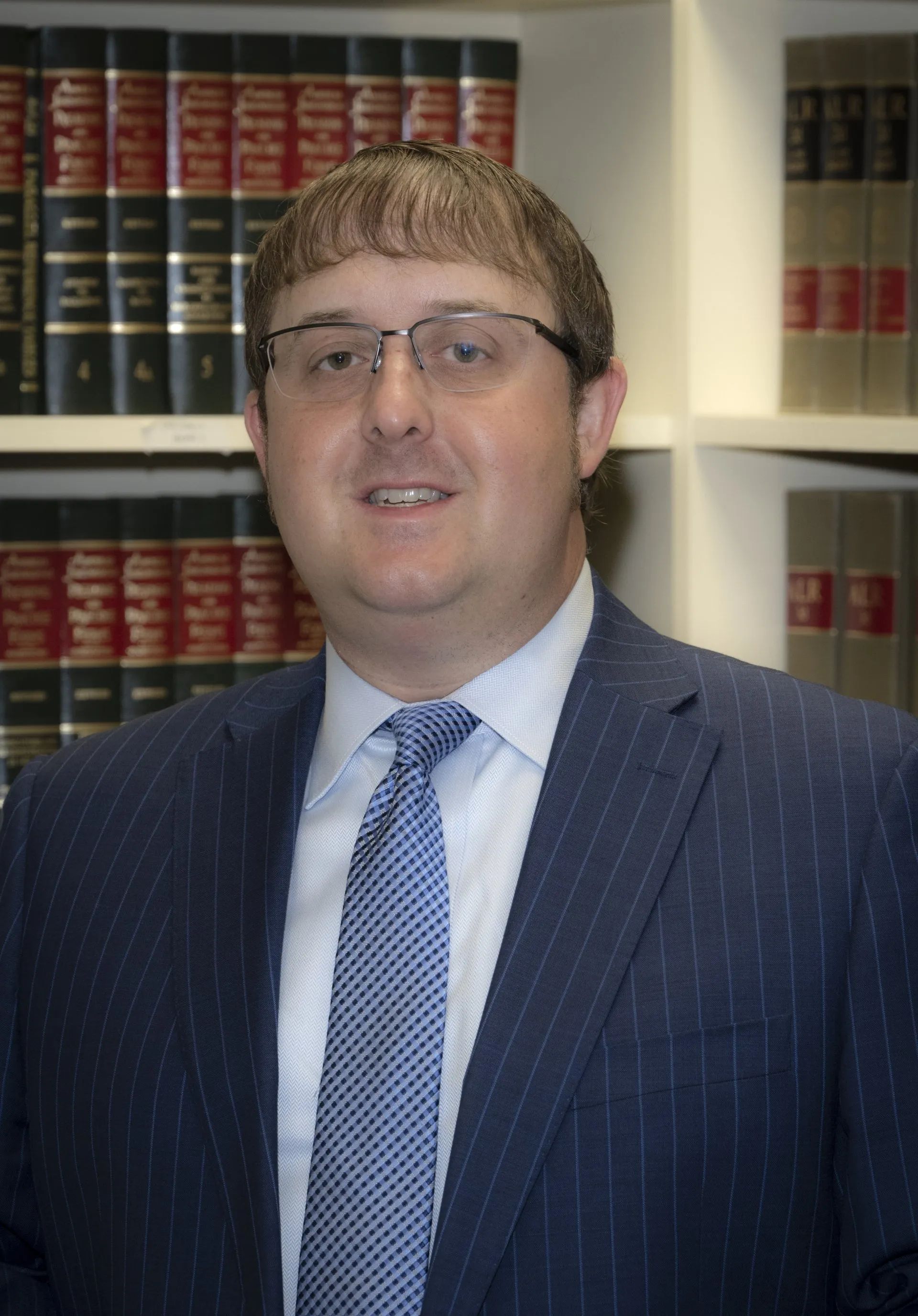 Man in suit and tie, smiling, in front of a bookshelf filled with law books.