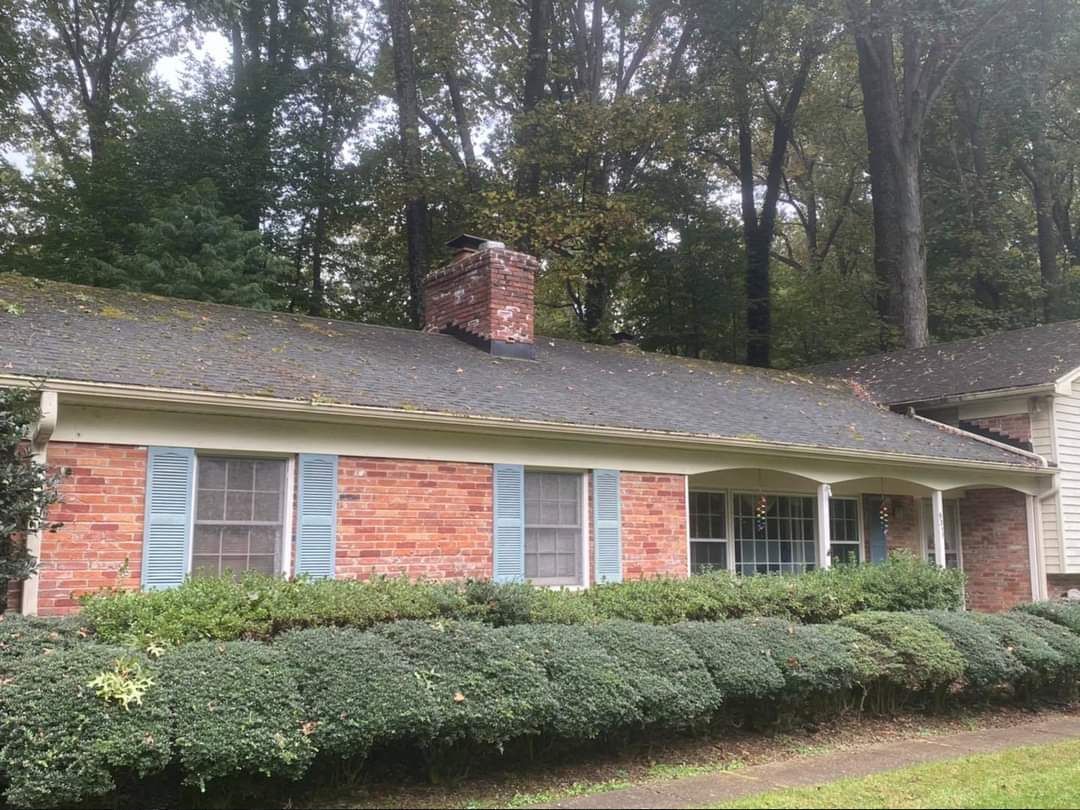 a brick house with blue shutters and a chimney on the roof surrounded by trees