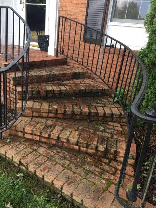 a brick walkway with a wrought iron railing and stairs leading up to a house
