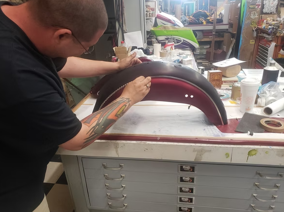 A man with a tattoo on his arm is working on a motorcycle fender