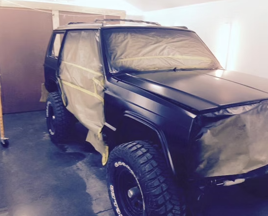 A black jeep is covered with a tarp in a garage