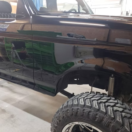 A black truck with a big tire is parked in a garage
