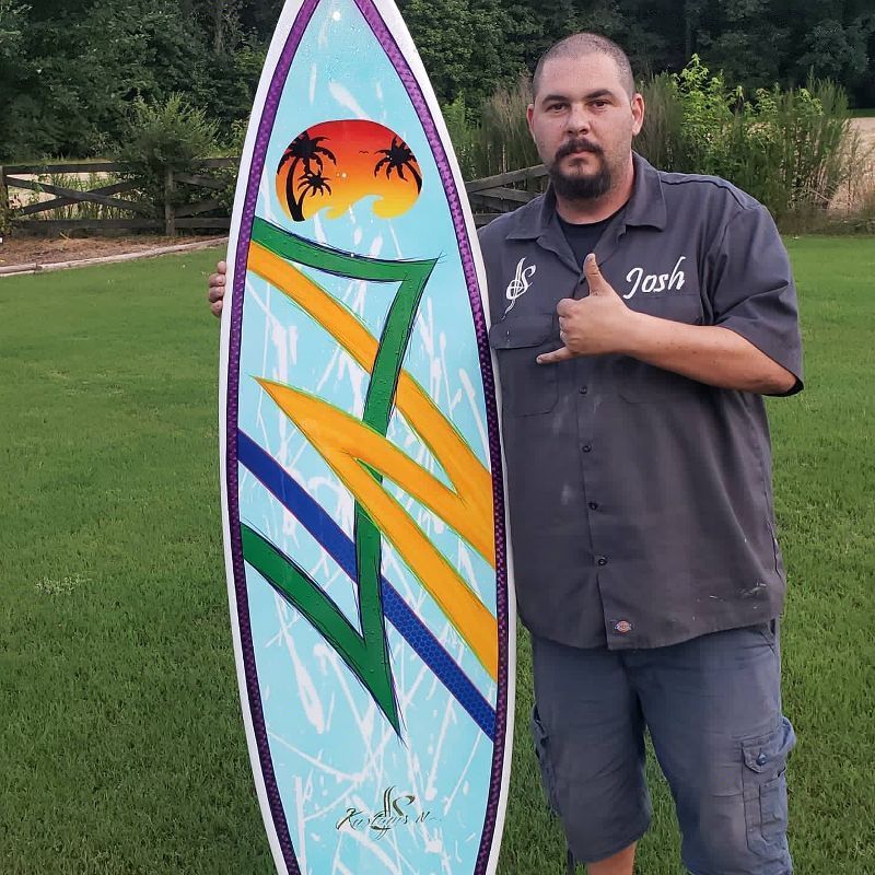 A man holding a surfboard with the name josh on his shirt