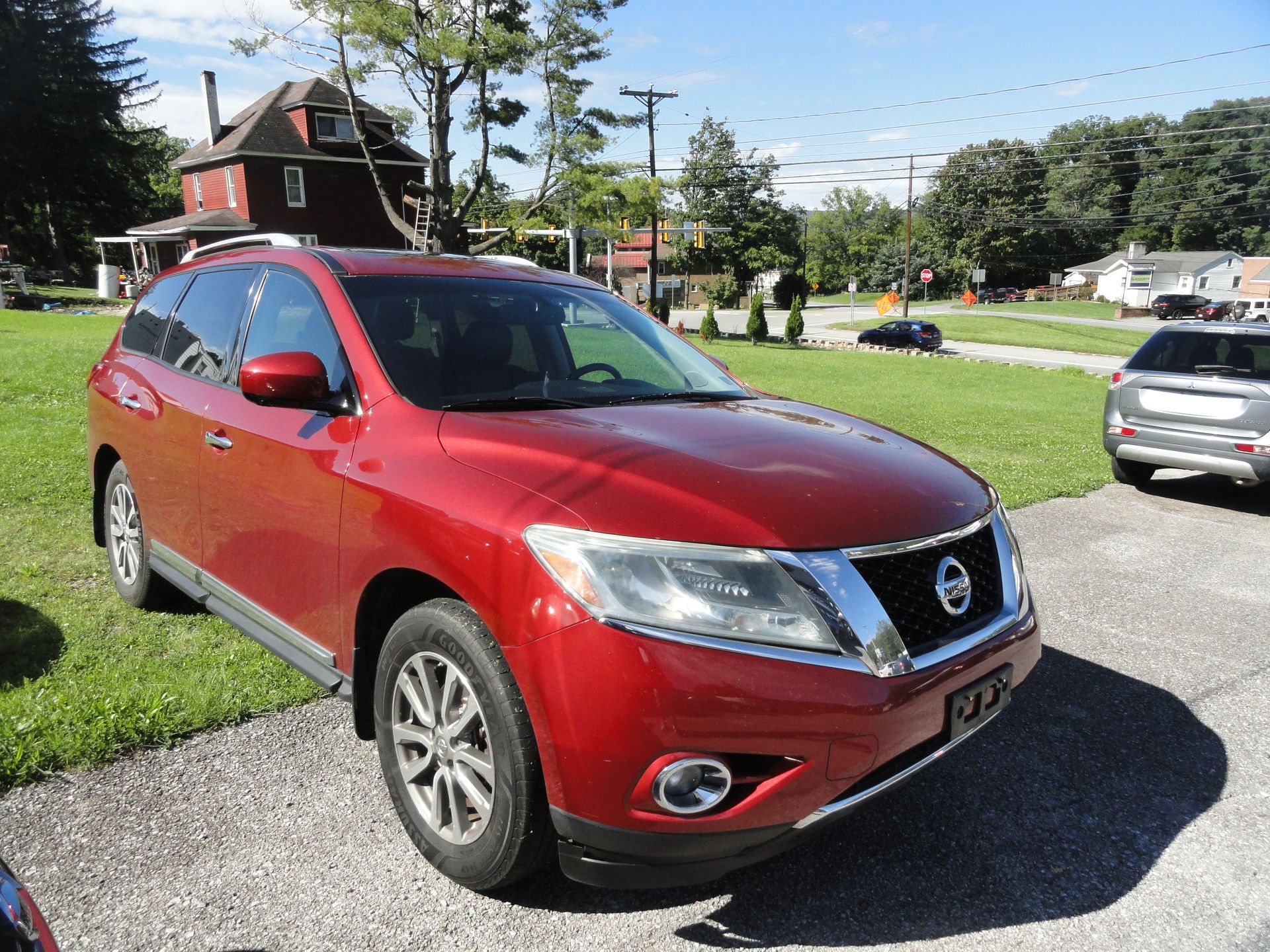 2015 Nissan Pathfinder 4WD parked on grass beside a red car in a lot, front three-quarter view