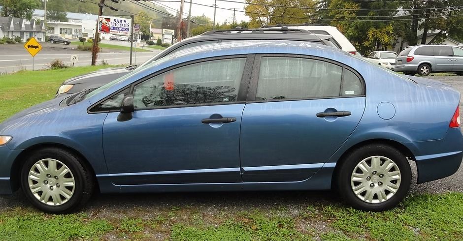 Blue sedan parked on wet grass beside a road on an overcast day