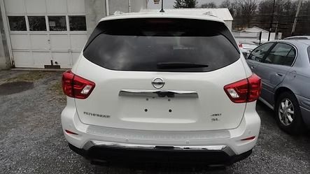 Rear view of a white Nissan SUV parked outside a garage on a wet driveway