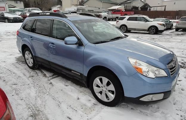 Blue station wagon parked on a snowy lot with other cars in the background