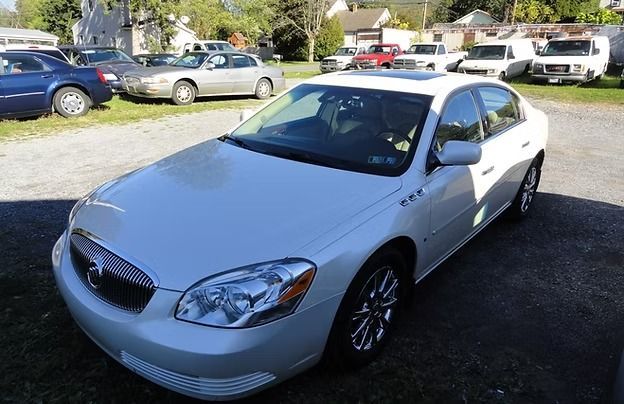 White sedan parked in a driveway, viewed from the front-left side on a sunny day.