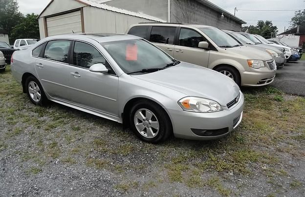 Silver sedan parked on gravel beside a beige minivan in a lot near a garage