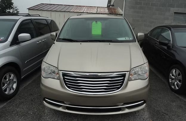 Beige minivan parked between two cars, with a green sale sign in the windshield.