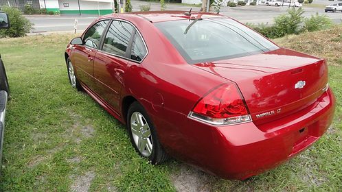 Red sedan parked on grass beside a sidewalk near a street
