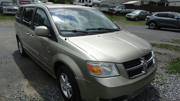 Silver minivan parked on a gravel lot with cars in the background.