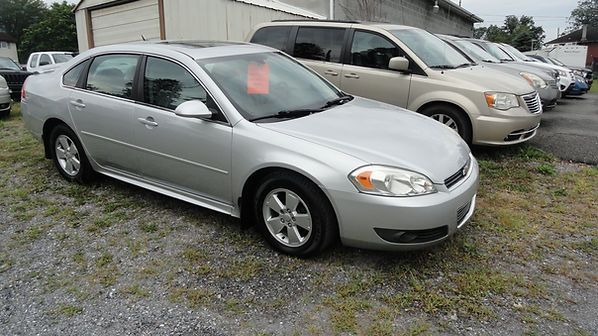Silver sedan parked on a gravel lot with other vehicles in the background