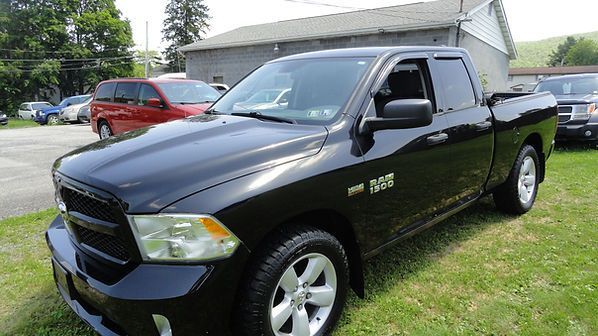 Black pickup truck parked on grass in front of a house, with a red vehicle in the background.