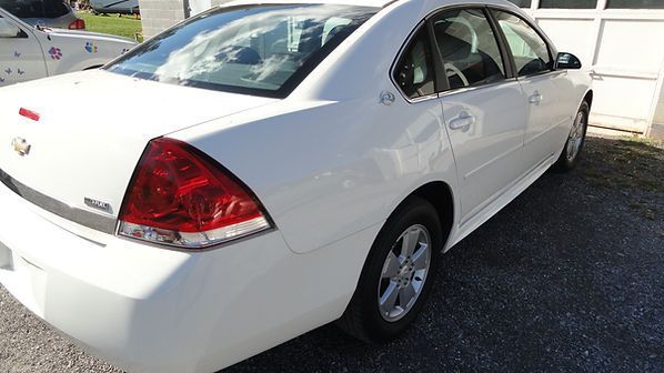 White sedan parked outdoors on a sunny street, rear three-quarter view.