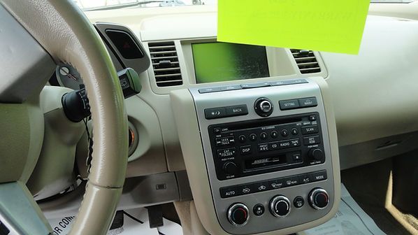 Car interior with steering wheel, center console, and a bright green paper note on the dashboard display.