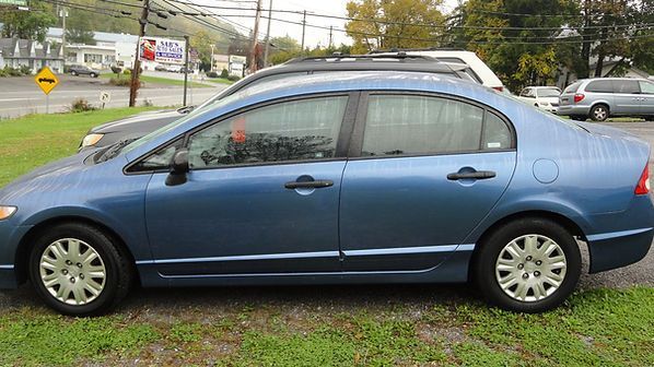 Blue sedan parked on grass beside a road under overcast skies