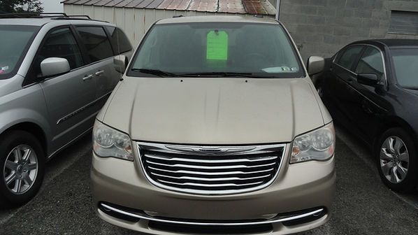 Front view of a beige minivan parked between two cars, with a green paper sign on the windshield.
