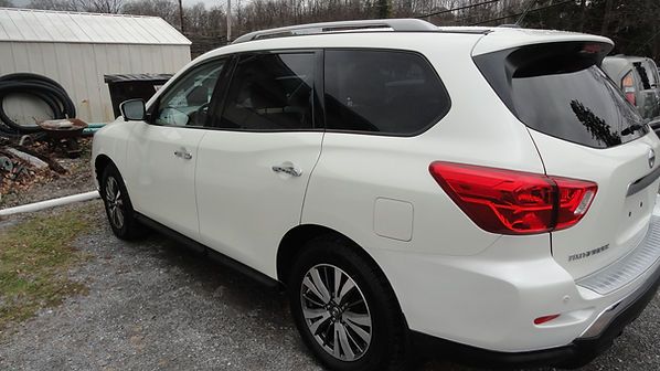 White SUV parked on a gravel driveway beside a shed in a rural yard