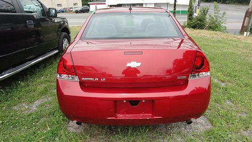 Rear view of a red sedan parked on grass beside a black vehicle and a sidewalk