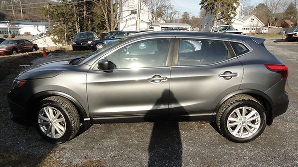 Gray SUV parked on a sunny lot, side view with trees and houses in the background