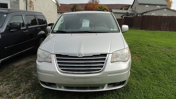 Silver minivan parked on grass beside a house, front view.