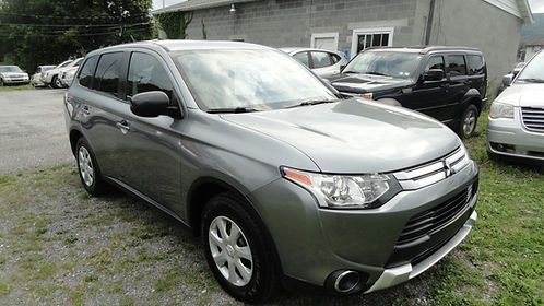 Gray compact SUV parked on grass in a lot, front-left view with other cars and a building behind it