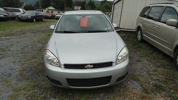 Silver Chevrolet sedan parked on a gravel lot with a red paper sign in the windshield