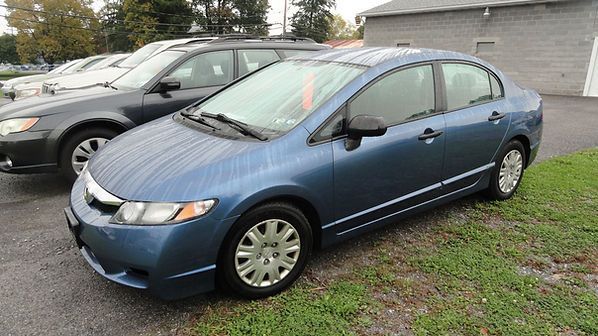 Blue sedan parked on wet grass beside a gray SUV near a house