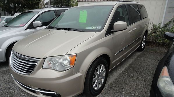 Beige minivan parked outdoors beside other cars, front-left view.