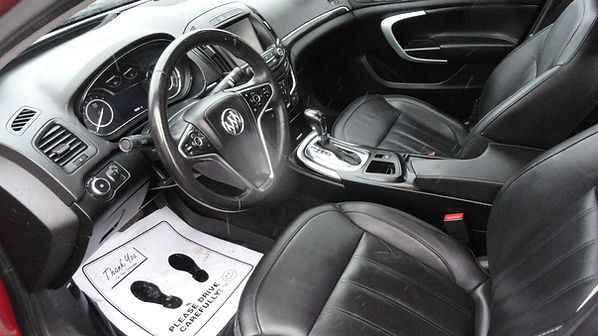 Black leather car interior with steering wheel, center console, and paper floor mat in the driver's footwell