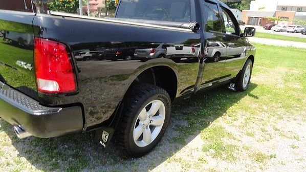 Black pickup truck parked on grass in a sunny yard, rear side view