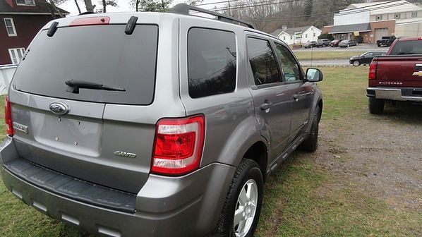 Gray SUV parked on a gravel lot beside a red truck near a building