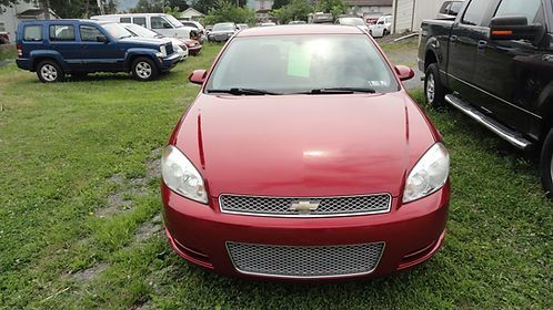 Red compact car parked on grass between other vehicles
