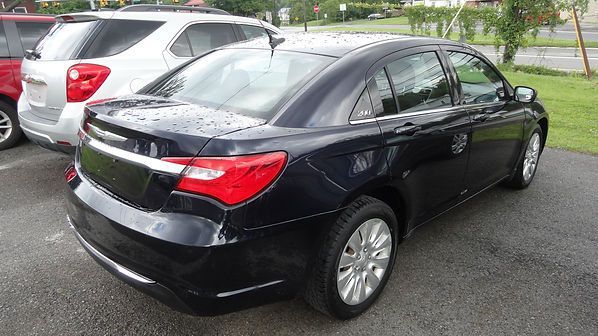 Black sedan parked in a wet lot beside a silver SUV, rear-left view