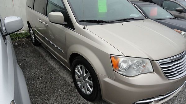 Beige minivan parked closely between cars on a wet lot