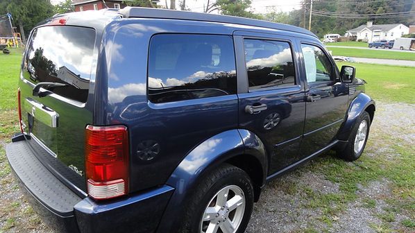 Dark blue SUV parked on grass, side and rear view with tinted windows and roof rack.