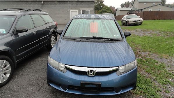 Blue Honda parked in a wet driveway in front of a garage, with two other cars nearby