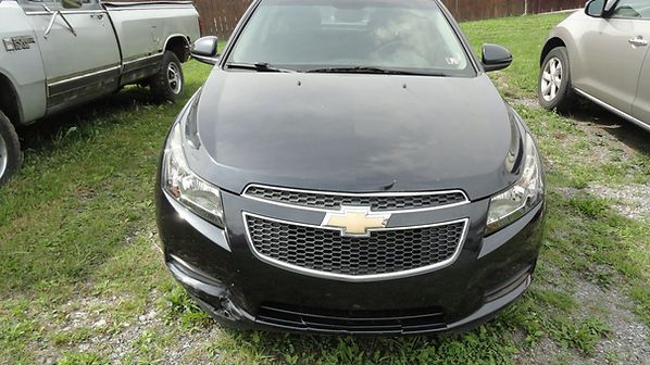 Front view of a black Chevrolet sedan parked on grass between two other vehicles