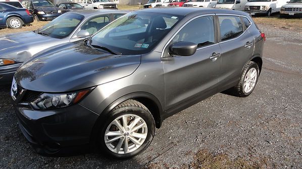 Gray compact SUV parked on a gravel lot, front-left view, with other cars in the background