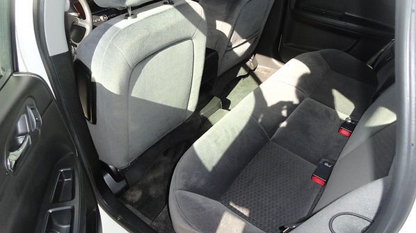 Rear car seat with black-and-gray upholstery and red seatbelt buckles inside a vehicle
