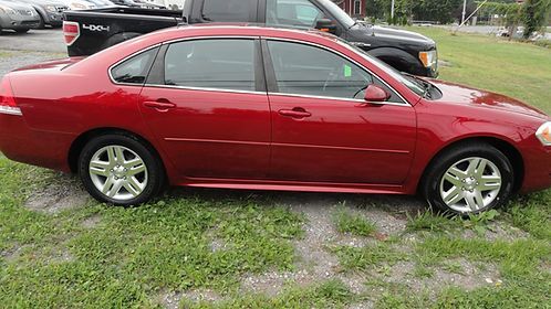 Red sedan parked on grass beside a black SUV near a road.