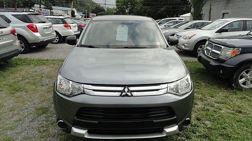 Front view of a silver Mitsubishi SUV parked in a grassy lot between other cars.