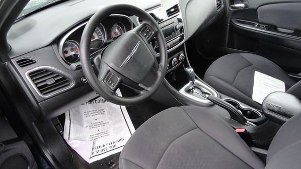 Interior of a black car with steering wheel, dashboard, center console, and papers on the driver’s seat floor