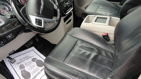 Black leather car interior with steering wheel, front seats, and a paper floor mat on the driver side