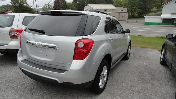 Silver SUV parked in a lot, rear view with tinted windows and wet pavement.